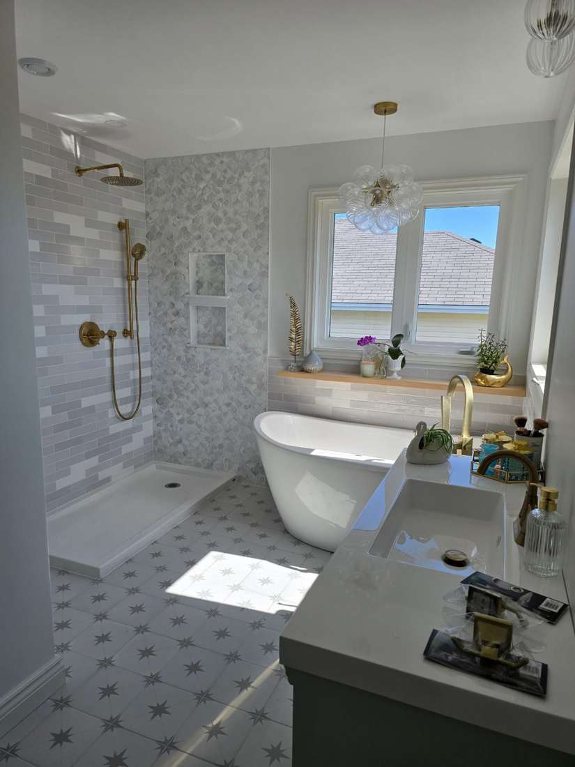 A completed Reshape bathroom renovation featuring a gold rainfall shower with marble hexagon tile, a freestanding soaking tub beneath a glass-bubble chandelier, star-patterned floor tile, and a quartz-topped vanity with gold fixtures.