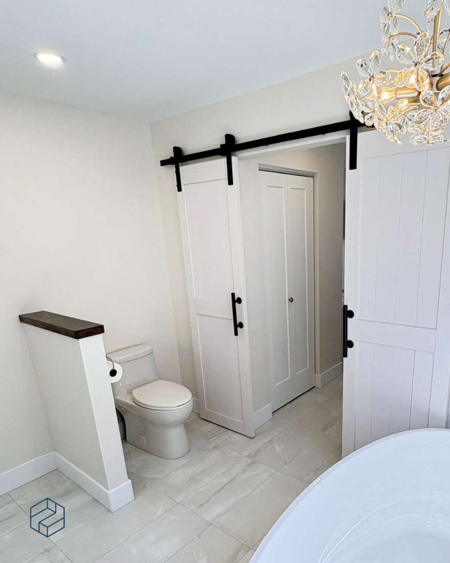 Water closet and linen storage behind sliding barn doors for privacy.