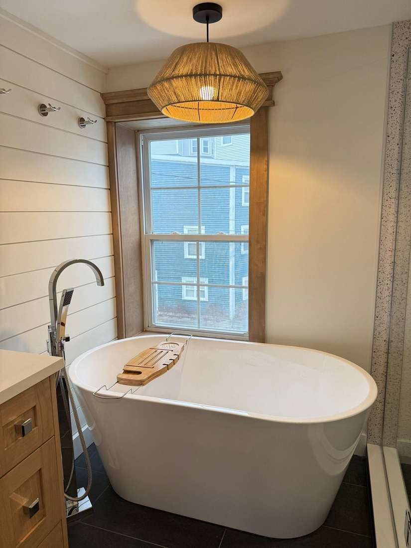 Freestanding soaking tub beneath a window and a woven rope pendant in the Bond Project bathroom.