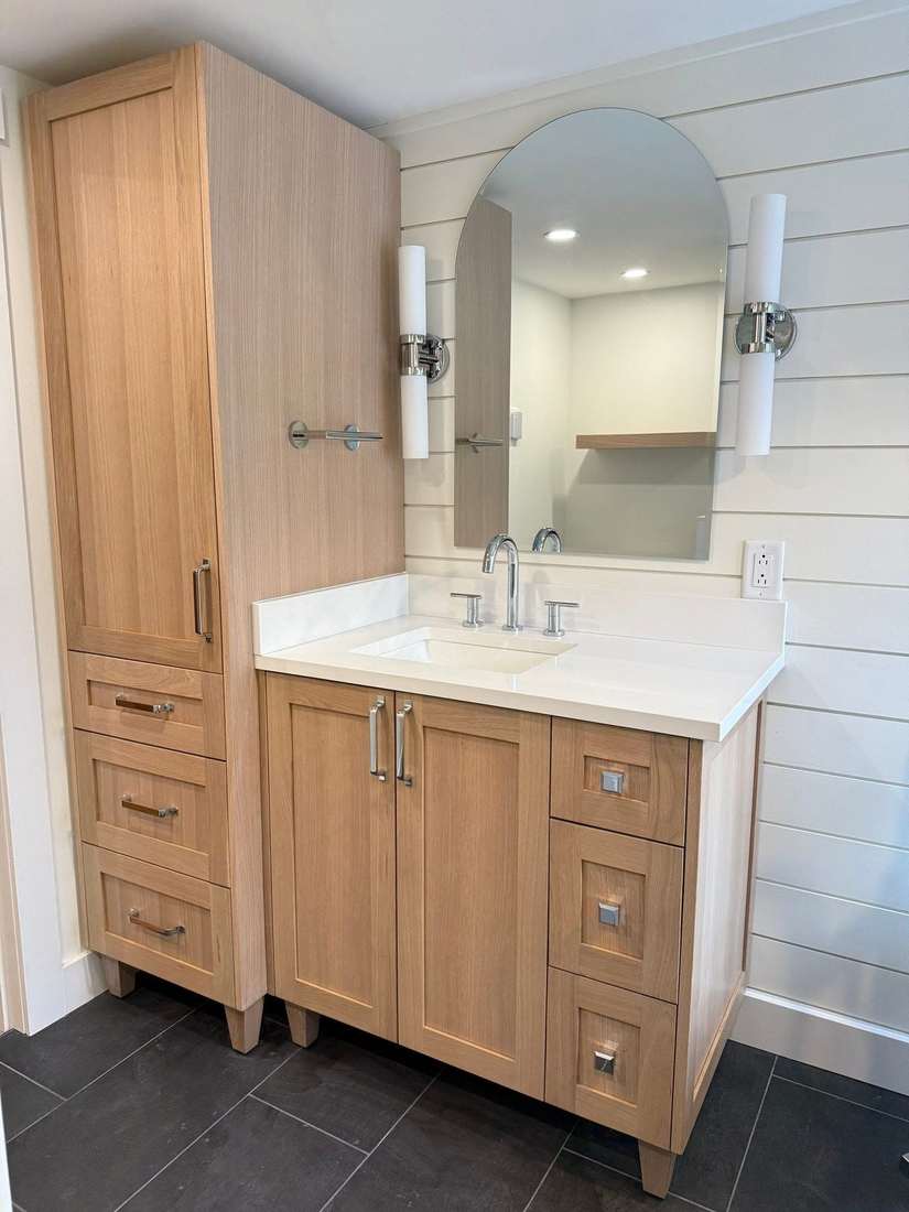 White-oak vanity with quartz top, arched mirror, and tall linen tower in the Bond Project.