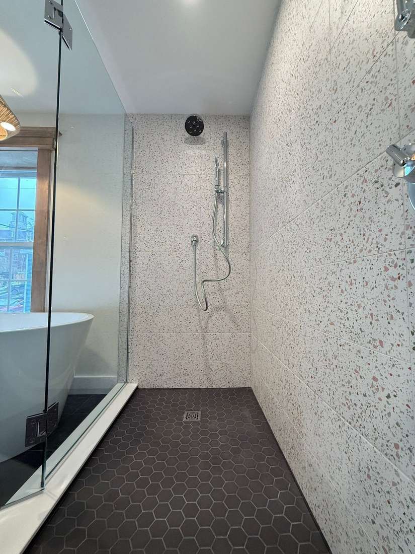 Curbless walk-in shower with terrazzo walls and dark hexagon floor tile in the Bond Project.